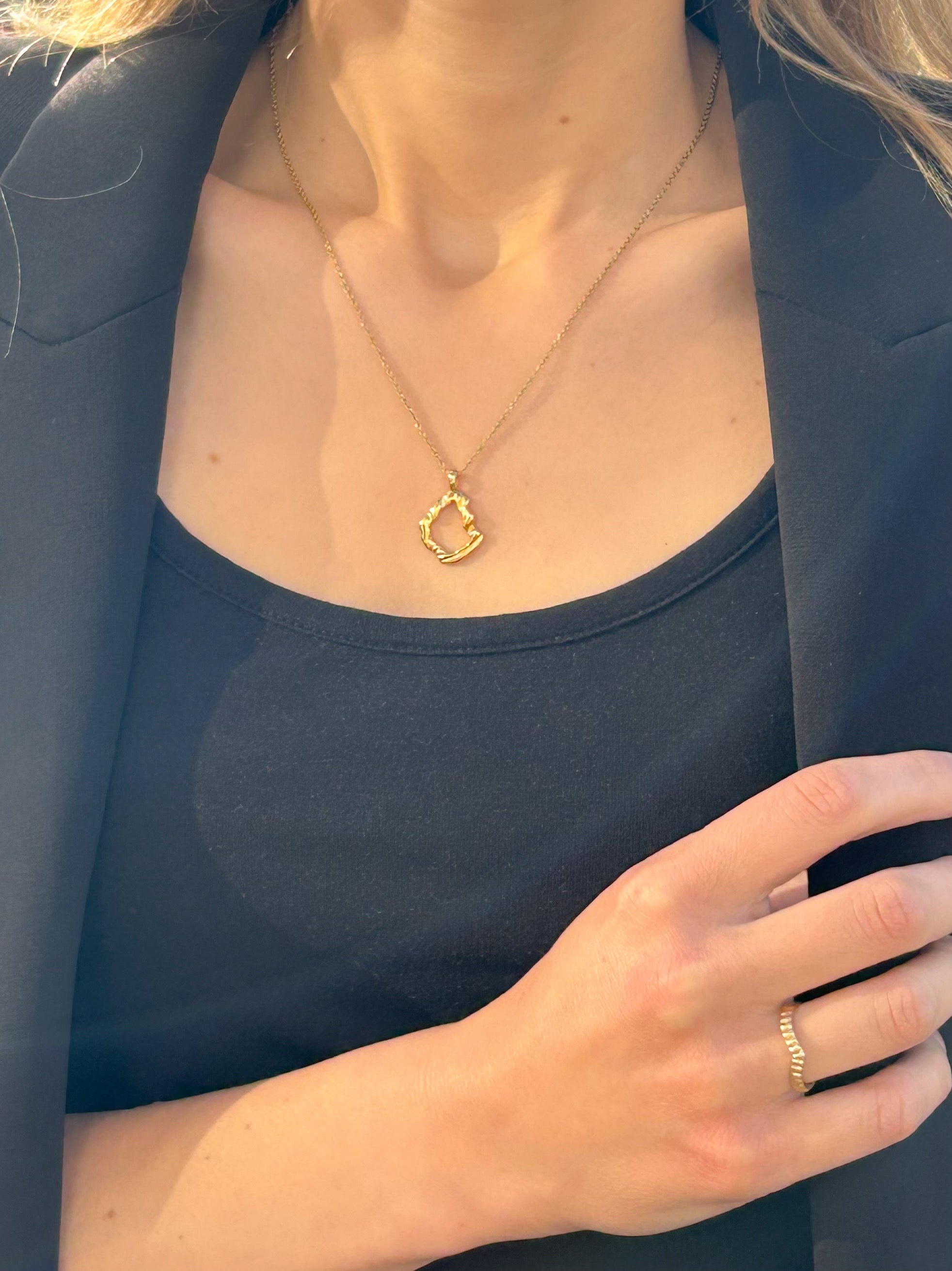 Shell fragment mirage pendant on model, wearing black top & blazer, & gold feather ring