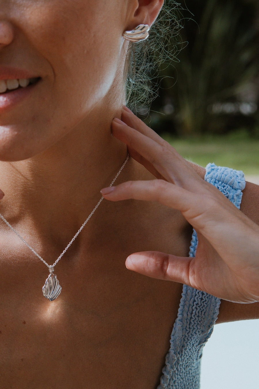 Silver shell fragment large stud earrings, on model, with matching necklace.  Outside in the sunlight.